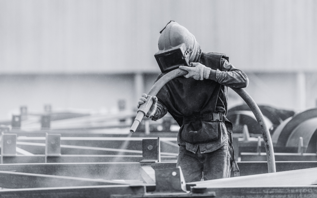 Sand blasting process, Industial worker using sand blasting process preparation cleaning surface on steel before painting in factory workshop.